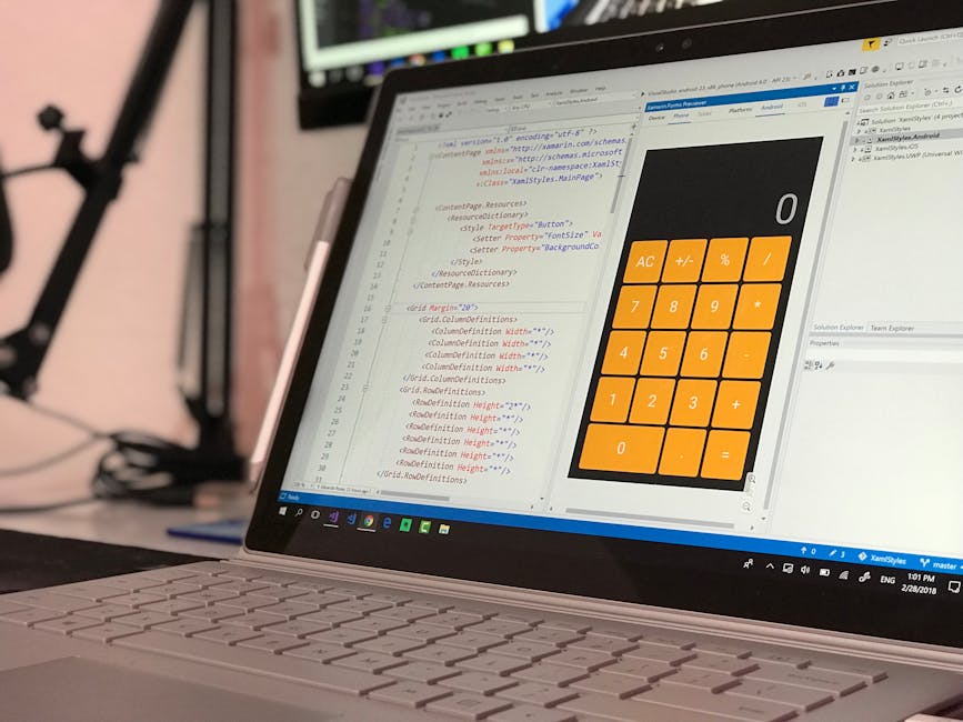 A close-up view of a silver laptop displaying a code editor with lines of HTML and CSS markup on the left side, and on the right side a large, orange calculator interface with black and white icons, i